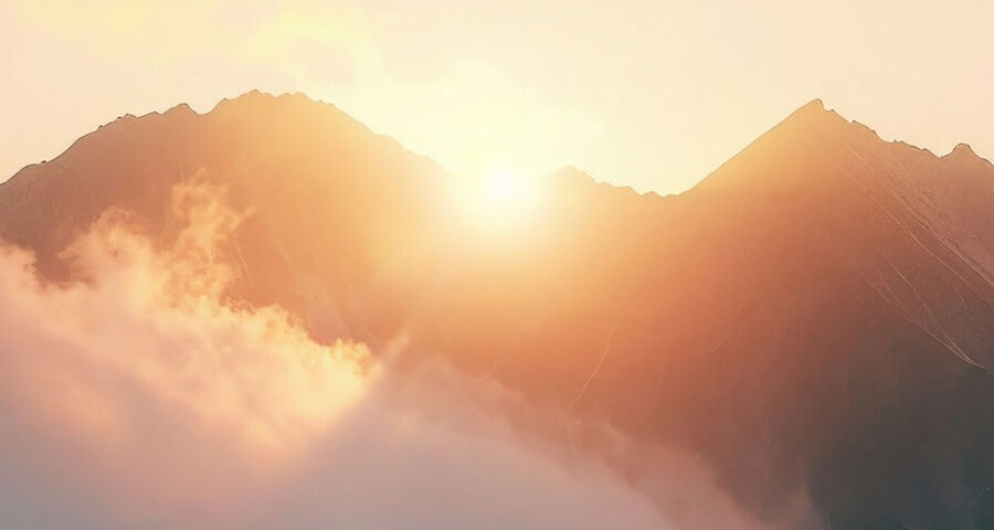 Die Sonne geht hinter nebeligen Berggipfeln auf, in warmem, goldenen Licht.
